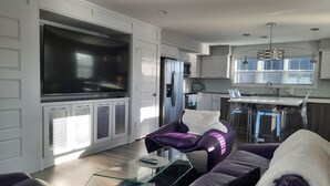 A modern living room with a large flat-screen TV, a glass coffee table, and a purple sofa. - Spacious 3 Room Condo Near Michigan's Piers and Waterways (Grand Haven)