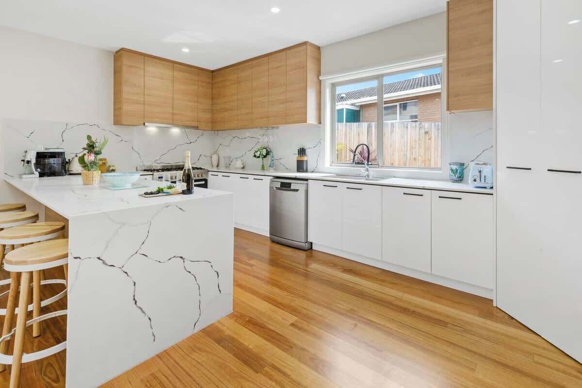 Een moderne keuken met witte kastjes, een marmeren eiland, houten krukken en een vaatwasser.