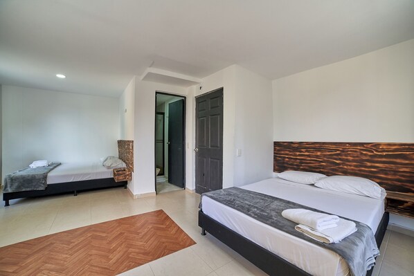 A bedroom with two beds, a wooden headboard, and a herringbone-patterned rug. - Farum Hotels (Medellín)
