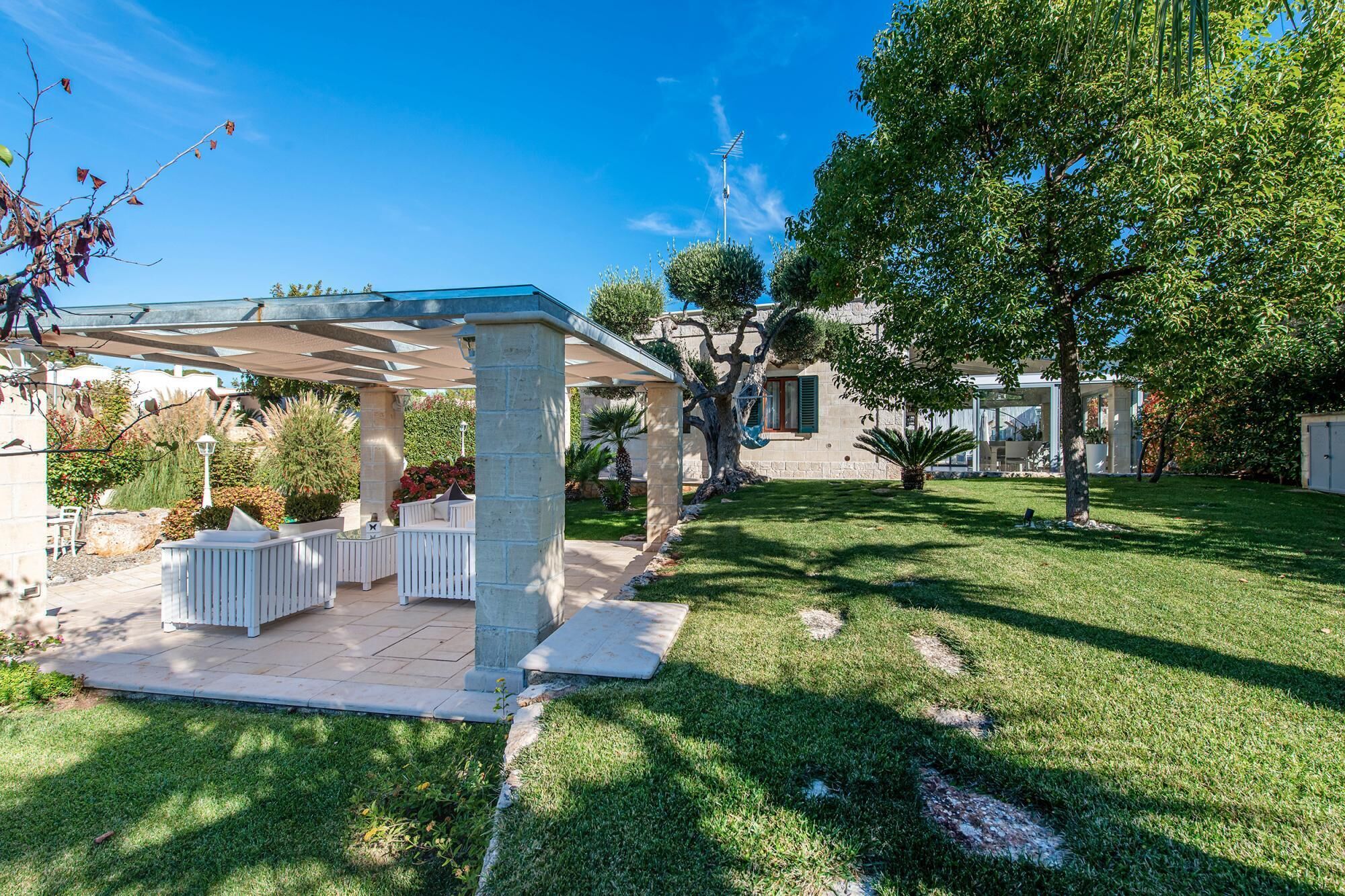 A covered patio area with outdoor furniture, a stone column, and a well-maintained lawn.