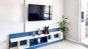 Ein modernes Wohnzimmer mit einem Wandfernseher, einem blau-weißen Konsolentisch und einer Topfpflanze.