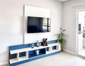 En moderne stue med et vægmonteret TV, et blå og hvidt konsolbord og en potteplante.