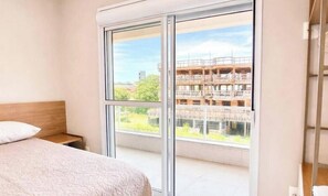 Un dormitorio con una ventana grande, una cama y vistas a un edificio en construcción.