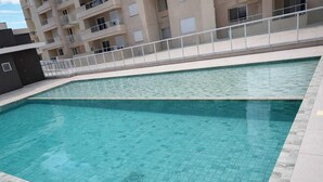 Ein Schwimmbad mit Fliesenboden, einer weißen Brüstung und einem Gebäude mit Balkonen im Hintergrund.