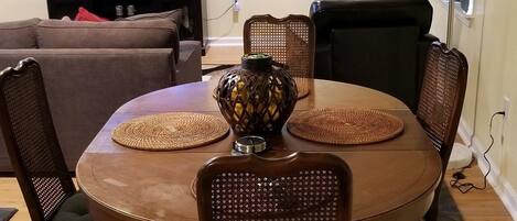 Zona pranzo con tavolo rotondo, sei sedie, un vaso decorativo, televisore e ventilatore a soffitto.
