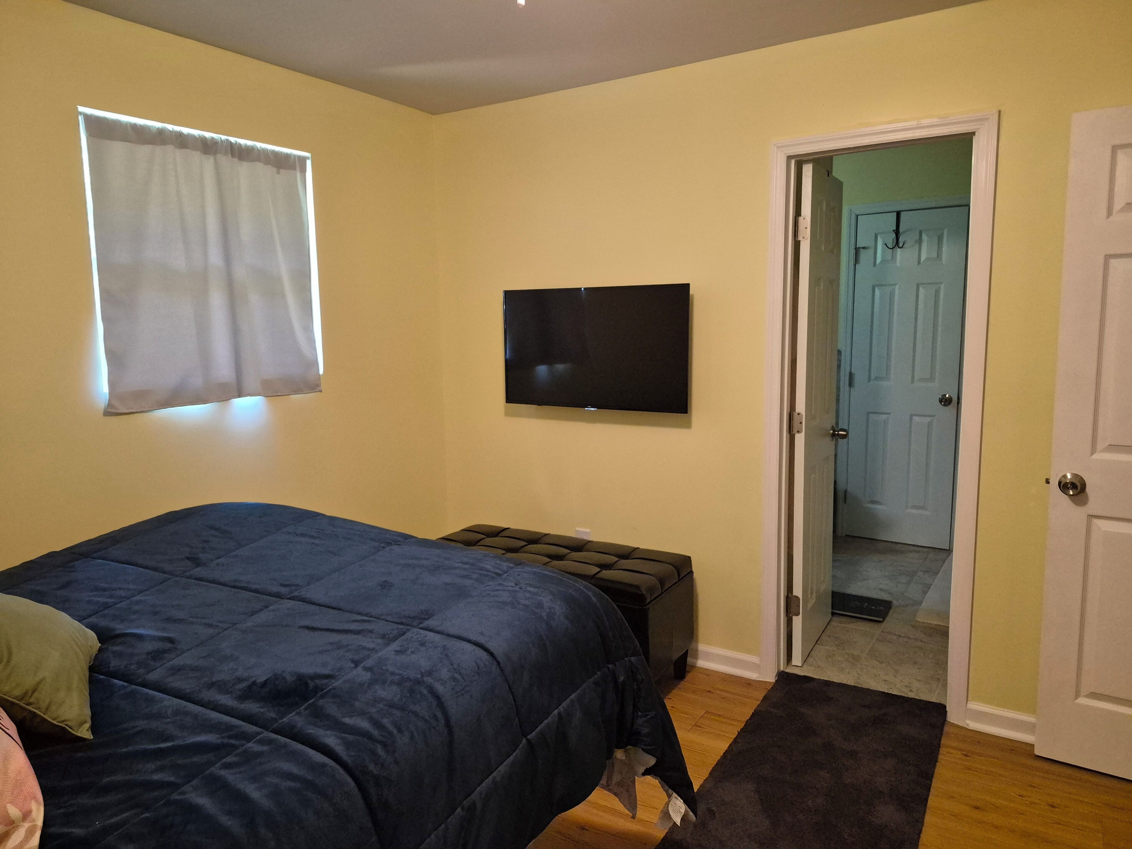 A bedroom with a bed, a television, a window with curtains, and a door leading to another room.