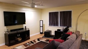 A living room with a flat-screen TV, a ceiling fan, a tall floor lamp, a sofa, and a window with curtains. - Close to Fort Eisenhower & Augusta Golf Course (Hephzibah)
