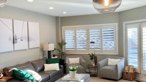 A modern living room with a sofa, ottoman, and armchairs, a dining area with a table and chairs, and a kitchen with a sink and countertop. - Deer Valley Condo w/ Private Hot Tub (Park City)