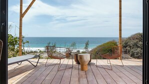 A wooden deck with a view of the ocean, two chairs, and a large planter. - Eolia Sustainable Design Hotel (Manta)