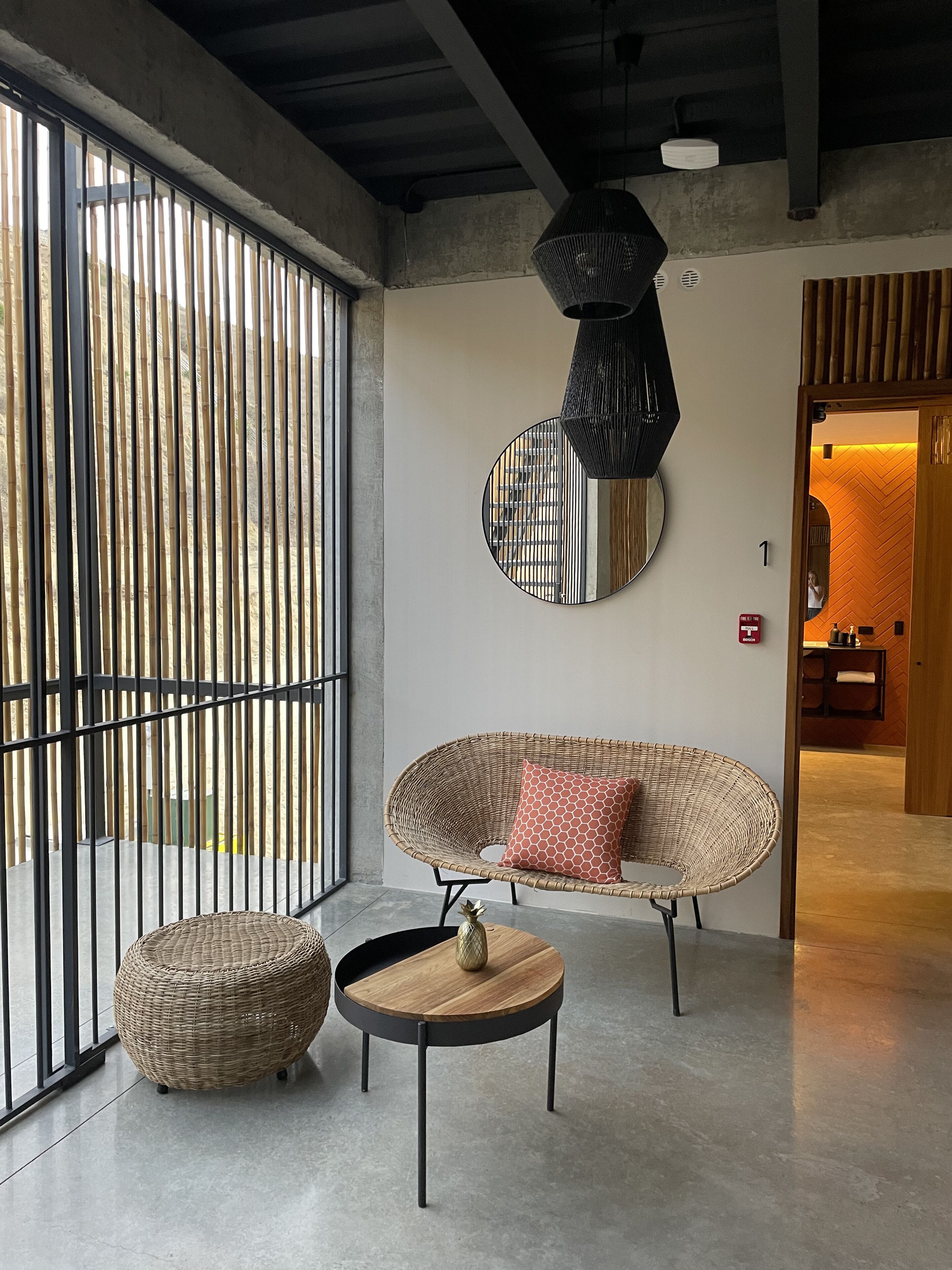Un intérieur moderne avec un canapé en osier, une table ronde et un grand miroir au mur.