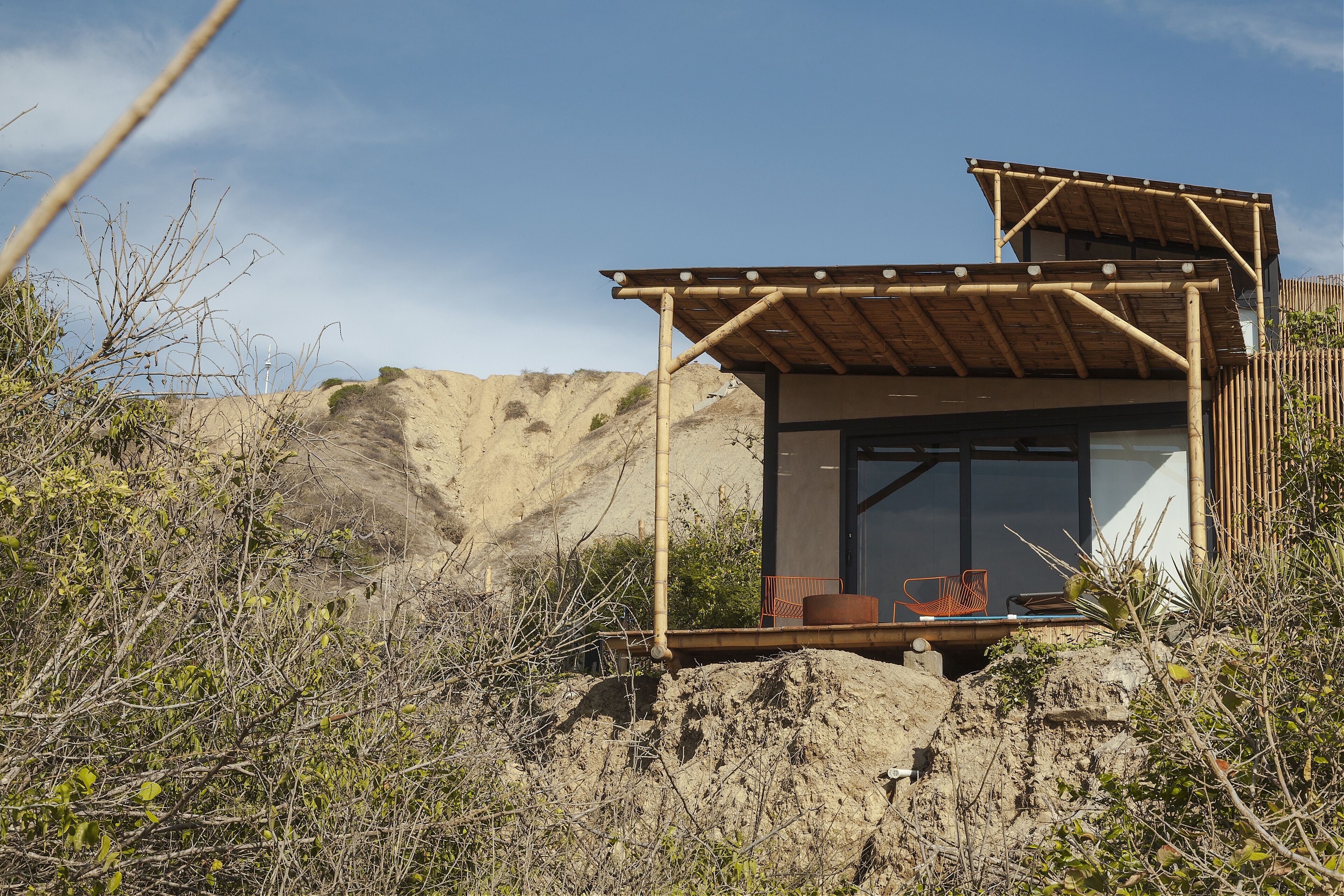 A small, single-story building with a wooden roof and large windows, surrounded by natural vegetation and a rocky landscape.
