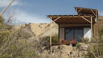 A small, single-story building with a wooden roof and large windows, surrounded by natural vegetation and a rocky landscape.