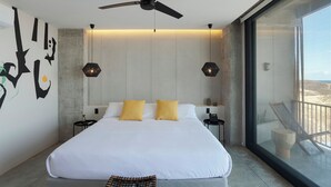 A modern bedroom with a large bed, two bedside tables, a ceiling fan, and a balcony with a view. - Eolia Sustainable Design Hotel (Manta)