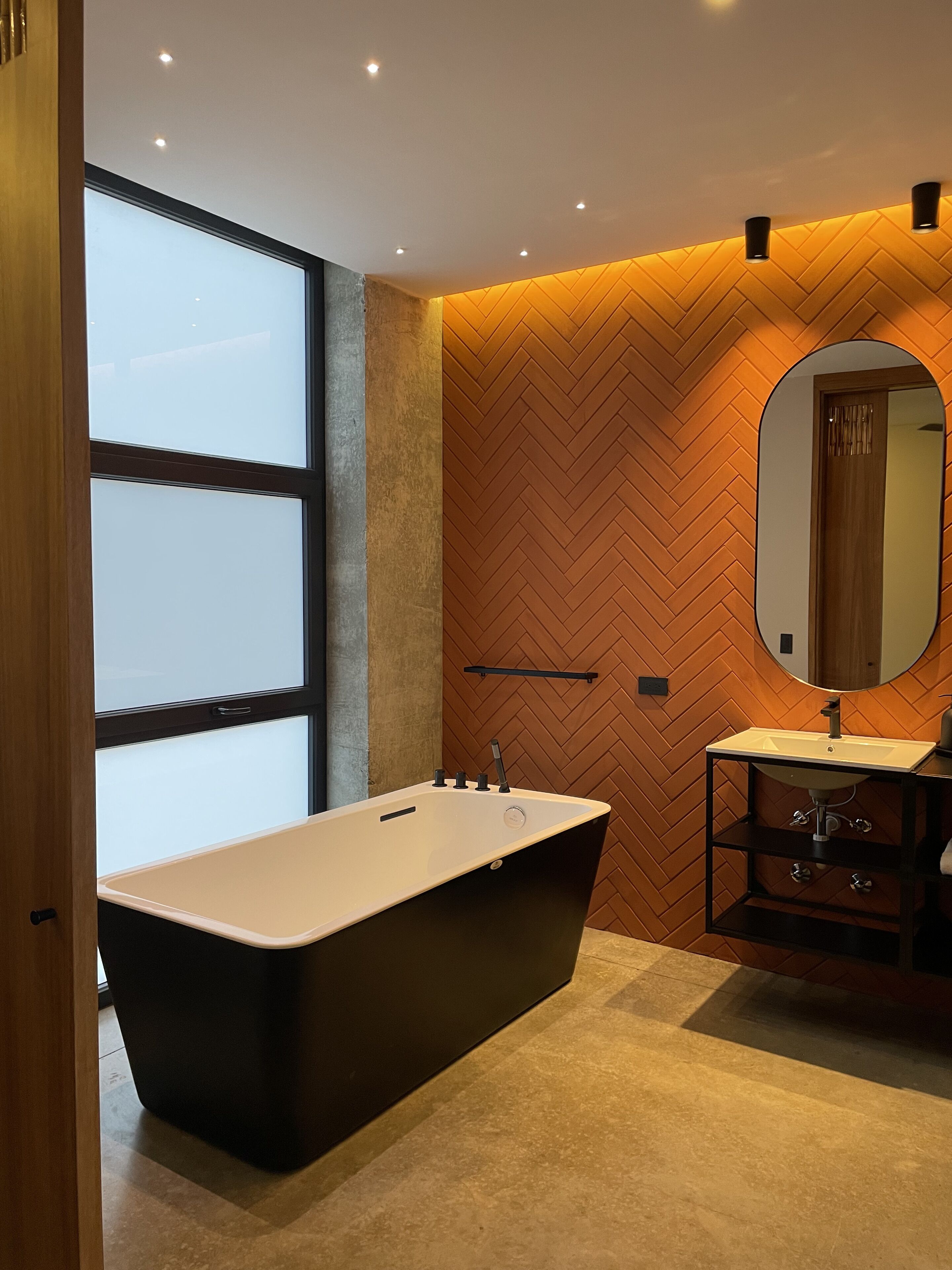 Un baño moderno con una bañera independiente, un espejo grande y un revestimiento de pared en patrón de espiga.