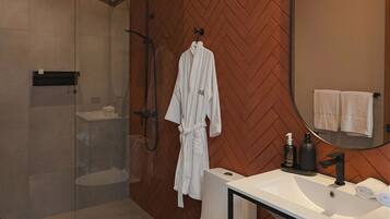 A modern bathroom with a glass-enclosed shower, a white toilet, a vanity with a mirror, and a shelf with towels and slippers.