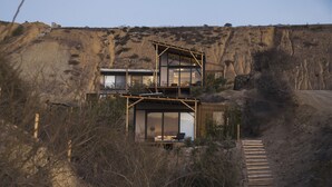 A two-story building with a glass facade, a wooden deck, and a dirt path leading to the entrance. - Eolia Sustainable Design Hotel (Manta)