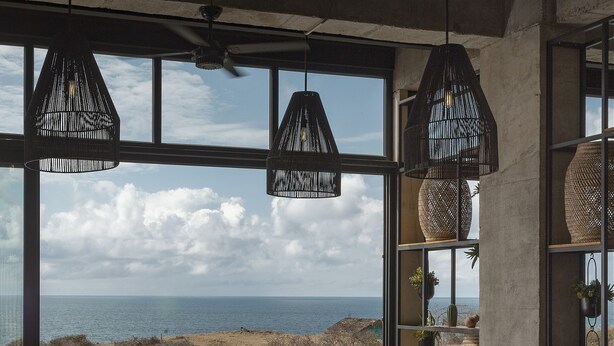 A modern living room with a large window overlooking a coastal landscape, a built-in pool, and a seating area with a coffee table. - Eolia Sustainable Design Hotel (Manta)