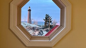Uitzicht door een zeshoekig raam op een vuurtoren, een besneeuwd landschap en een gebouw met rode daken.