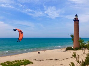 A beach with a lighthouse and a kite in the sky.