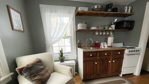 A compact kitchen with a white stove, wooden cabinets, and a small window with white curtains. - Getaway Near Mass MoCA, Great Hiking, Scenic Views (Stamford)