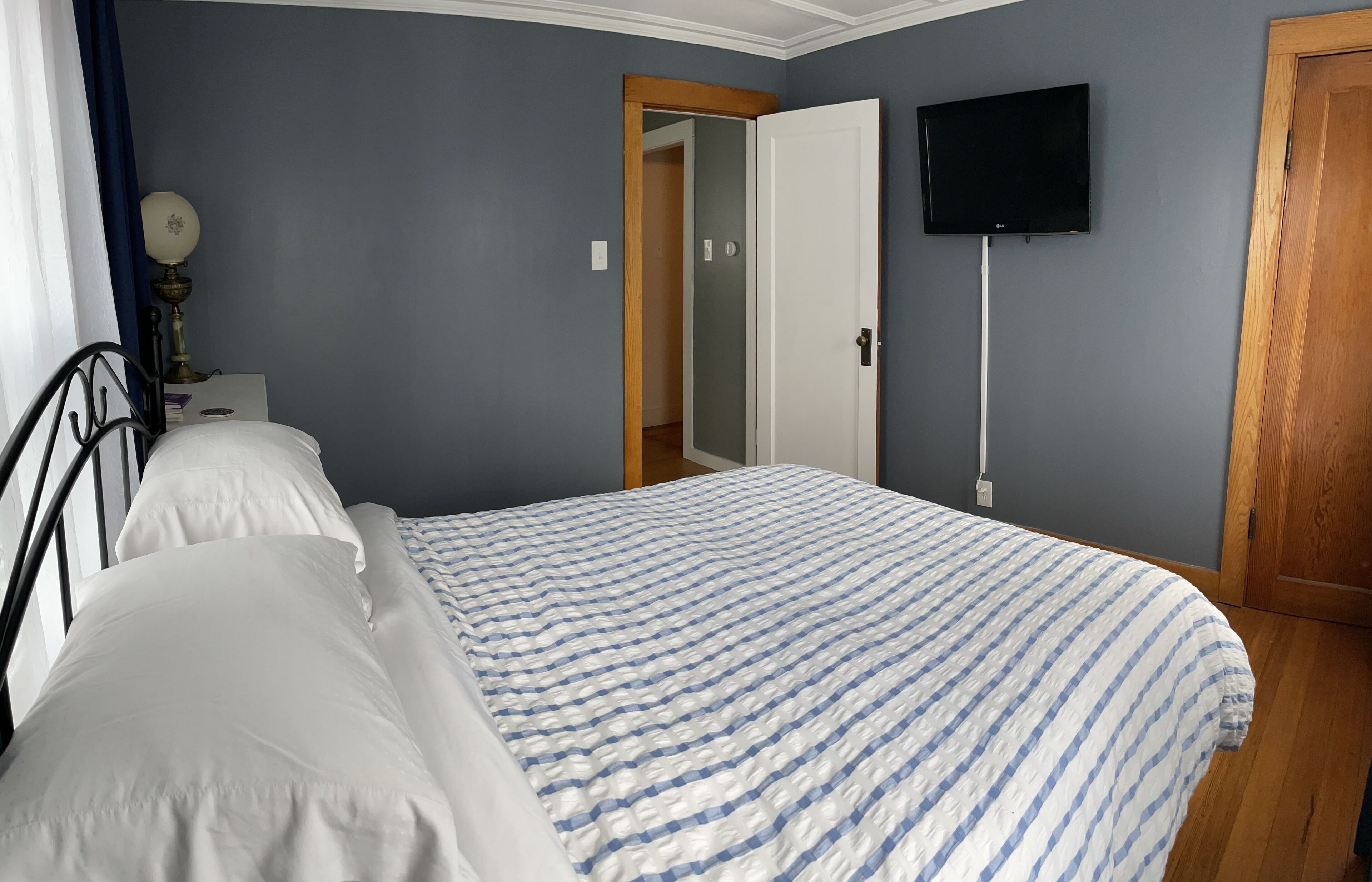 A bedroom with a bed, a television mounted on the wall, and a door leading to another room.
