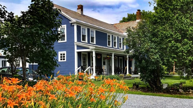 A two-story blue house with a porch, surrounded by a garden with orange flowers. - Getaway Near Mass MoCA, Great Hiking, Scenic Views (Stamford)