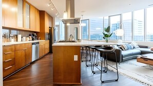 A modern kitchen with wooden cabinets, a central island, and a dining area with a sofa and chairs. - 2BR Penthouse | Gym | Bellevue | Sophari Towers E (Bellevue)