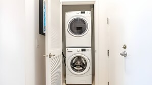 A laundry room with two stacked front-loading washing machines and a door with a handle. - 2BR Penthouse | Gym | Bellevue | Sophari Towers E (Bellevue)