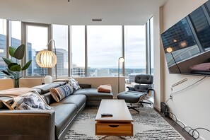 A modern living room with a sofa, a coffee table, and a TV mounted on the wall. - 2BR Penthouse | Gym | Bellevue | Sophari Towers E (Bellevue)