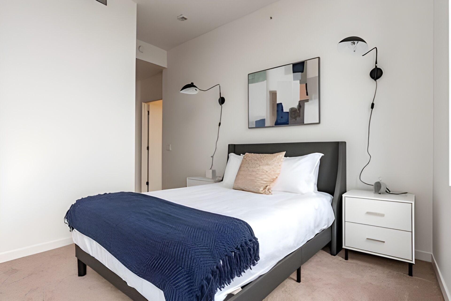 A modern bedroom with a bed, bedside tables, a nightstand, a mirror, and a wall-mounted lamp.