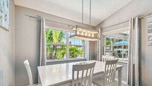 Un comedor con una mesa y sillas blancas, ventanas amplias con cortinas y una lámpara colgante.