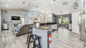 Amplia sala de estar con una isla grande, cocina con encimera negra y comedor con cojines estampados.