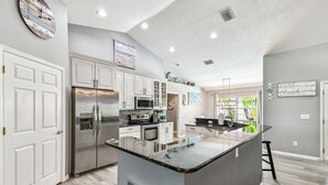 Una cocina moderna con armarios blancos, un refrigerador de acero inoxidable, un microondas y una isla grande con encimera de vidrio.