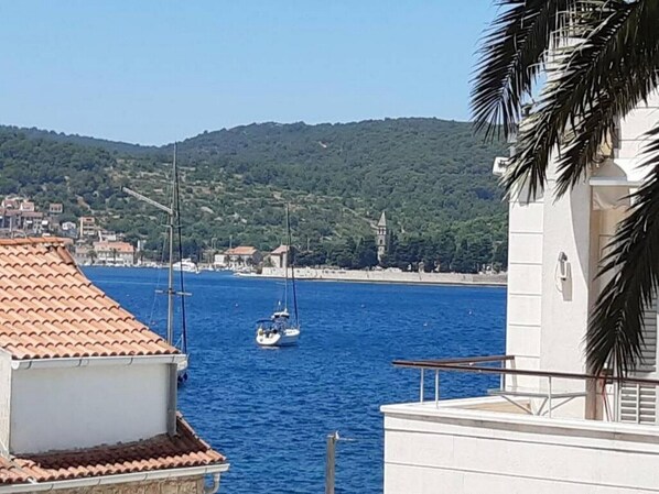 A coastal building with a tiled roof, a view of the sea, and a sailboat in the distance.