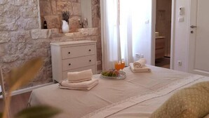 A hotel room with a stone wall, a white dresser, a bed with a white bedspread, a vase with dried plants, and a candle. - Casa Ruben - Two Bedroom Holiday Home with Sea View (Vis)