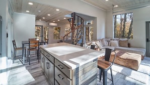 A modern interior with a central island, a staircase, and a cozy seating area. - Skywalk Treehouse: 4 Treehouses Linked by Bridges (Sevierville)