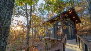 A wooden deck leading to a cabin surrounded by trees. - Skywalk Treehouse: 4 Treehouses Linked by Bridges (Sevierville)