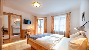 A bedroom with a wooden bed, a desk, a chair, a television, and a bathroom visible through an open door. - Apartment Carolina 185A (Ortisei)