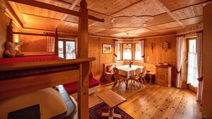 A wooden cabin interior with a dining area, a bed with red bedding, and a wooden ceiling. - Apartment Carolina 185A (Ortisei)