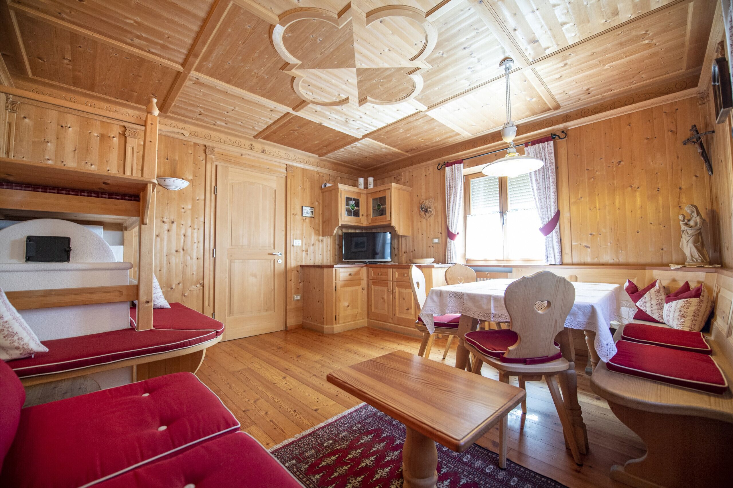 Ein Holzblockhaus-Interieur mit Essbereich, Küche und einer gemütlichen Sitzecke mit roten Kissen.