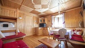 Ein Holzblockhaus-Interieur mit Essbereich, Küche und einer gemütlichen Sitzecke mit roten Kissen.