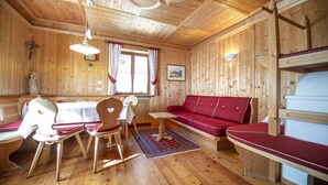 Ein Holzblockhaus-Interieur mit Esstisch, Stühlen, einer roten Couch und einem Schlafstockbett.