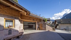 Ein traditionelles Steinhaus mit einer Holzfassade, einem überdachten Eingang und einer Steinsitzbank davor.