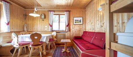 Een houten cabin met een eethoek, een rode bank en een houten plafond.