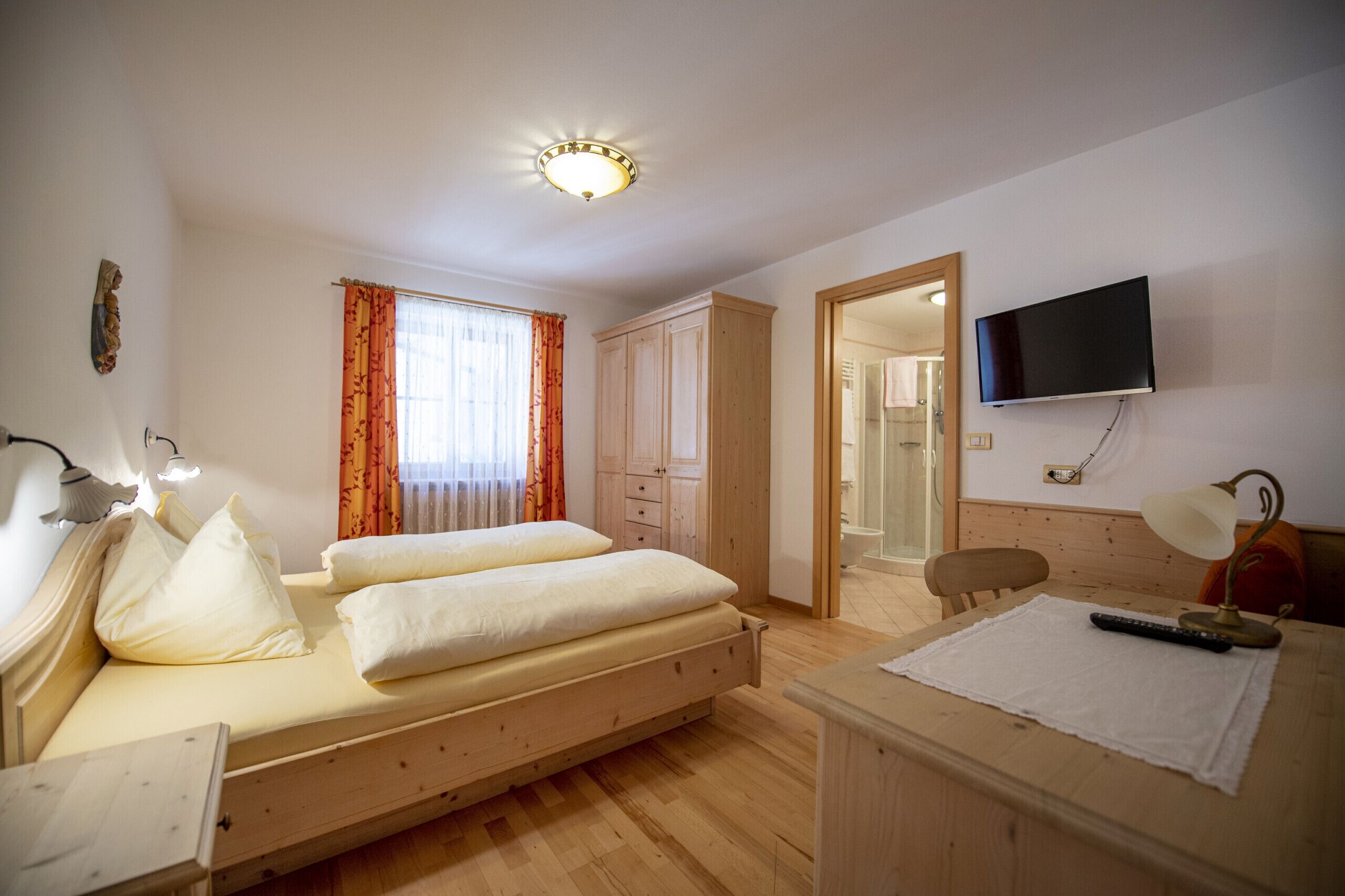 Een slaapkamer met twee bedden, een televisie, een bureau, en een badkamer die door een open deur zichtbaar is.