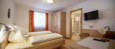 Een slaapkamer met twee bedden, een televisie, een bureau, en een badkamer die door een open deur zichtbaar is.