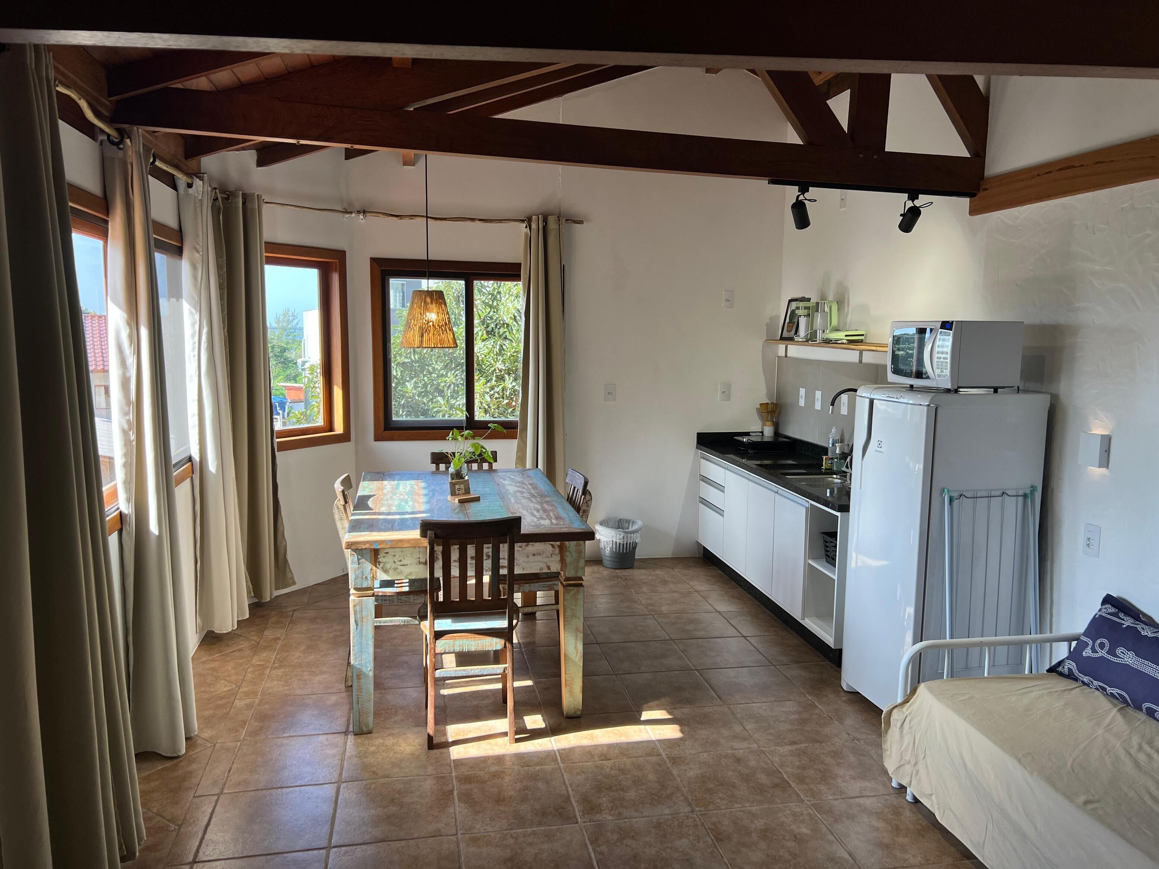 A compact kitchen with a dining table, chairs, a refrigerator, and a microwave.