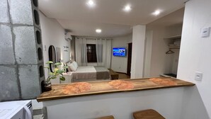 A compact hotel room with a kitchenette, a bed, a TV, and a small seating area. - Studios Aromas do Campeche - Floripa (Florianópolis)