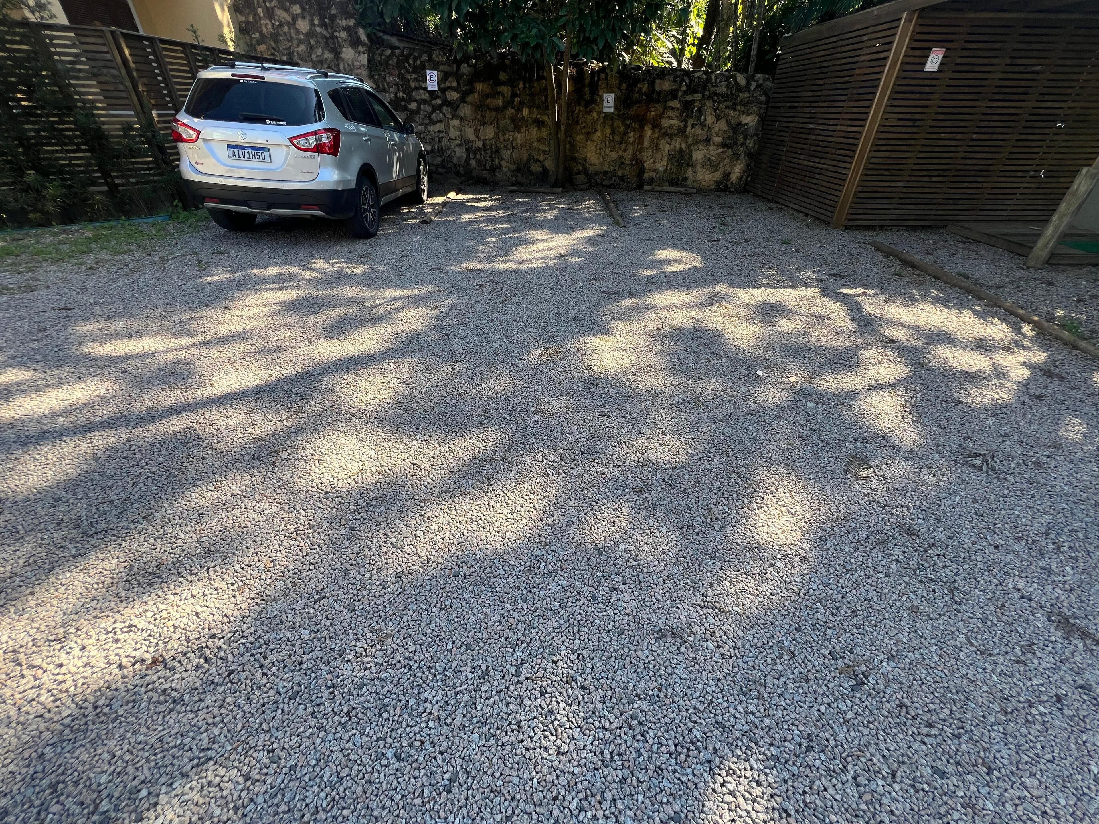 A gravel driveway with a parked car and a stone wall.