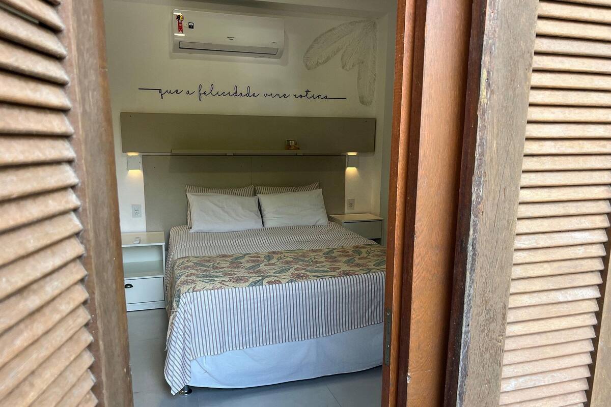 Une chambre à coucher comprenant un lit, une table de chevet, un climatiseur fixé au mur et un mur décoratif orné d’un motif de feuilles.
